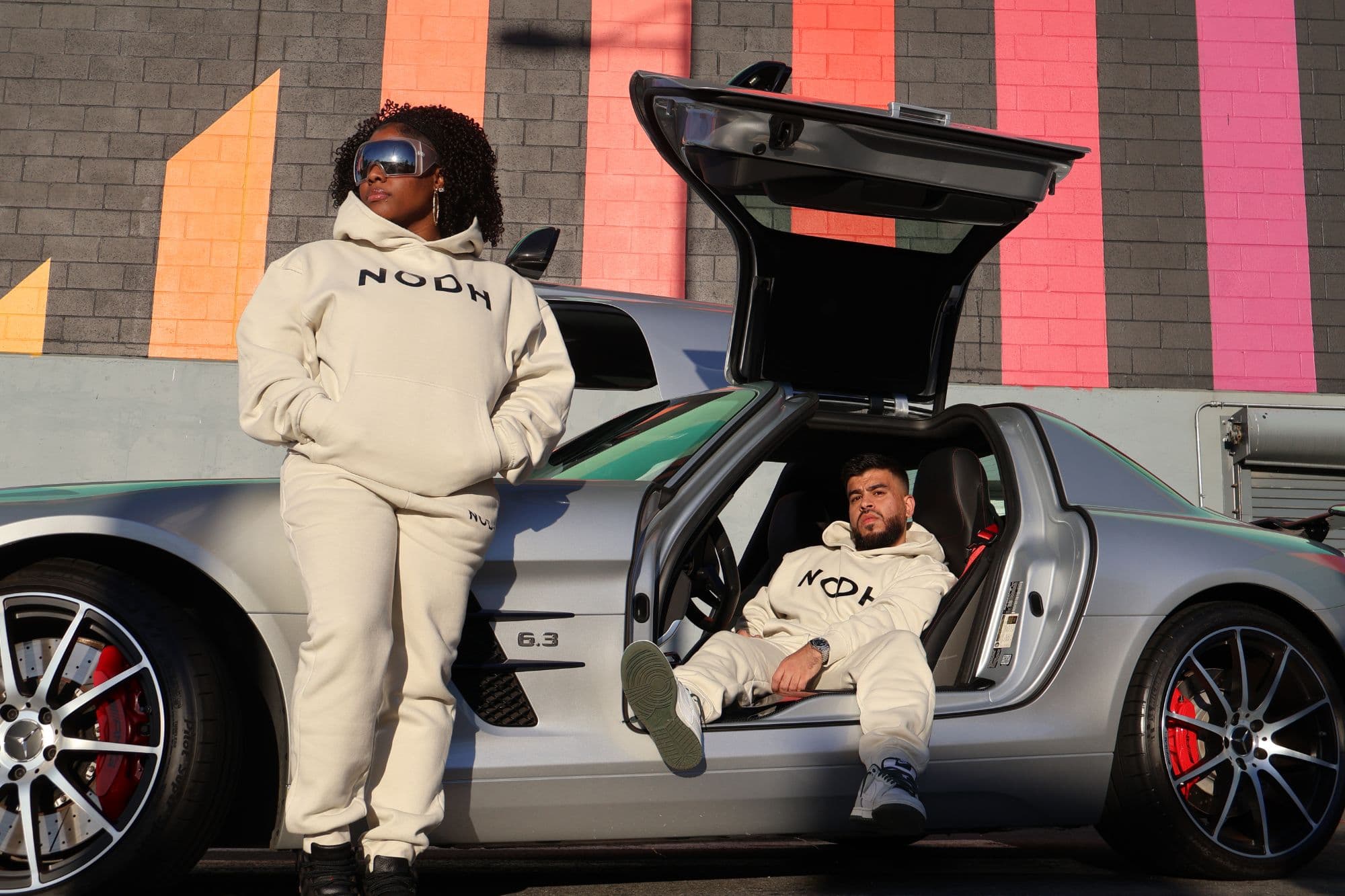 Two people in the NODH cream set beside a gullwing Mercedes